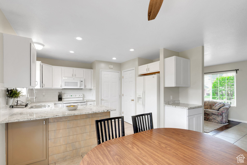 Kitchen with a peninsula, light tile patterned flooring, white appliances, tasteful backsplash, and a sink