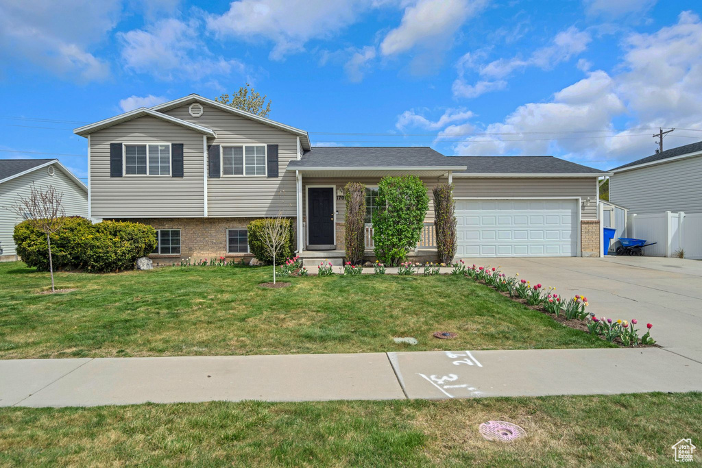 Split level home featuring brick siding, a front lawn, an attached garage, and concrete driveway