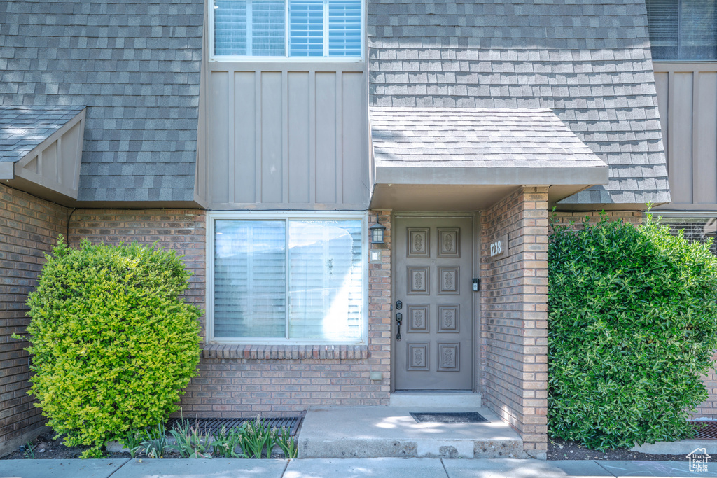 Property entrance featuring brick siding, a shingled roof, and board and batten siding