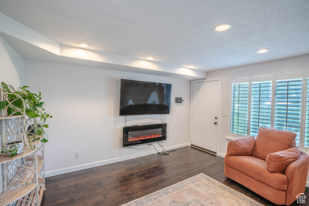 Living area with baseboards, recessed lighting, a glass covered fireplace, and dark wood-style floors