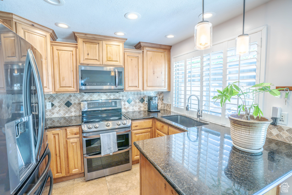 Kitchen with light brown cabinetry, tasteful backsplash, a sink, dark stone countertops, and appliances with stainless steel finishes