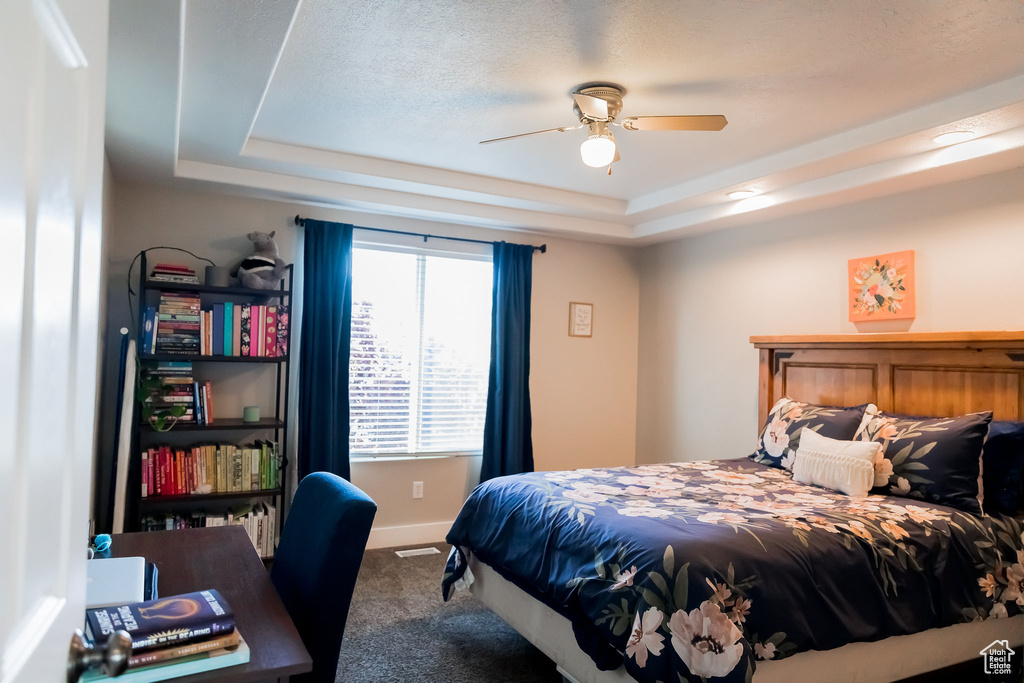 Bedroom with baseboards, carpet flooring, a raised ceiling, and a ceiling fan