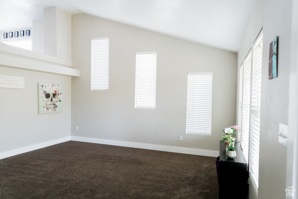 Unfurnished room with baseboards, vaulted ceiling, and dark carpet