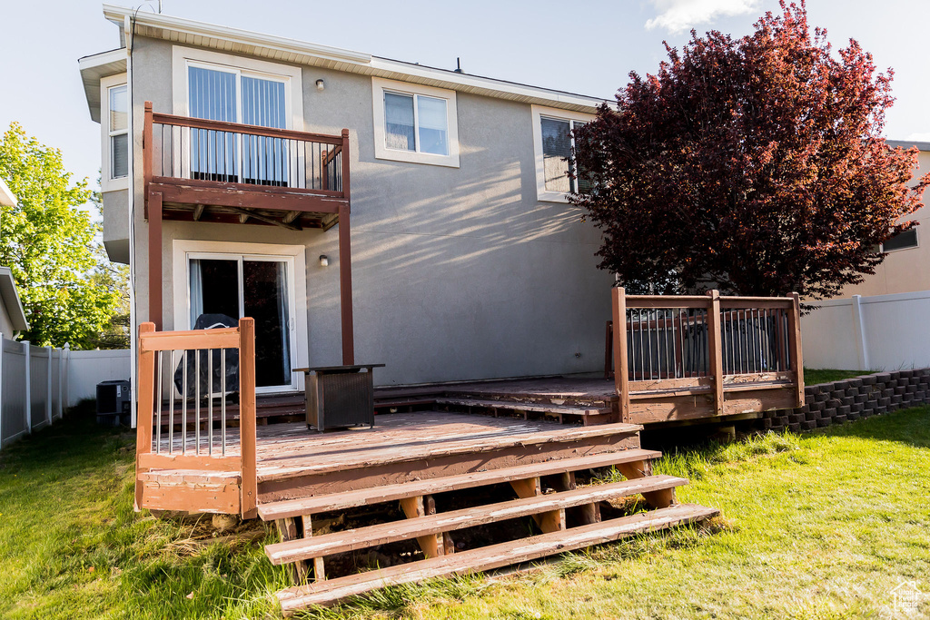 Back of house featuring a fenced backyard, a wooden deck, a yard, and a balcony
