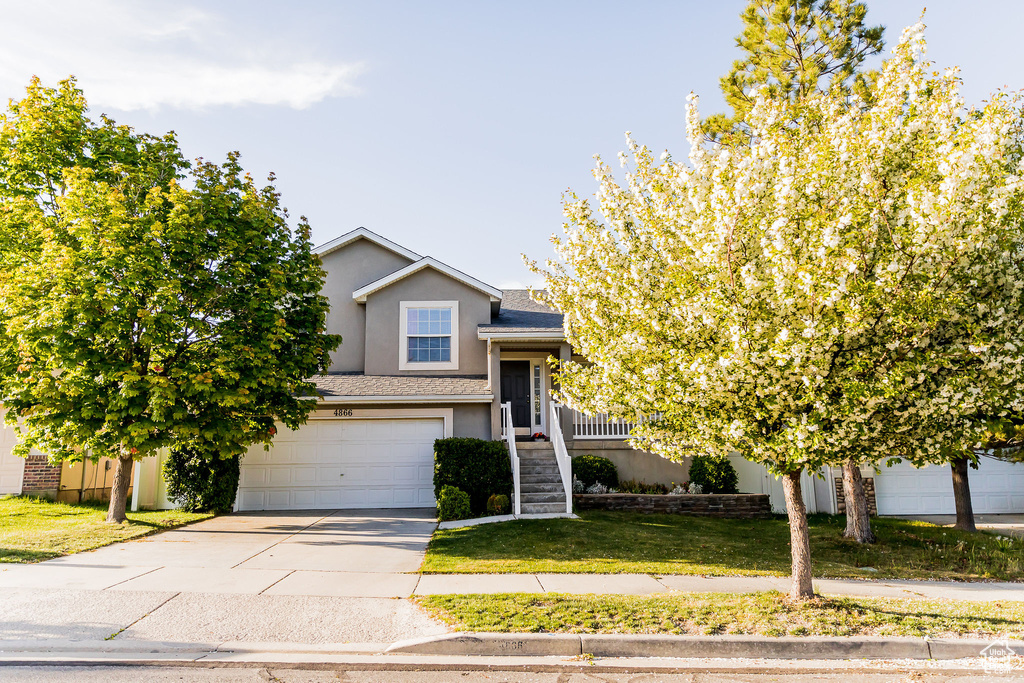 View of front of house featuring an attached garage, stucco siding, concrete driveway, and a front lawn