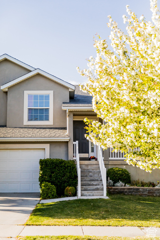 View of front of property featuring a garage, driveway, a front lawn, and stucco siding