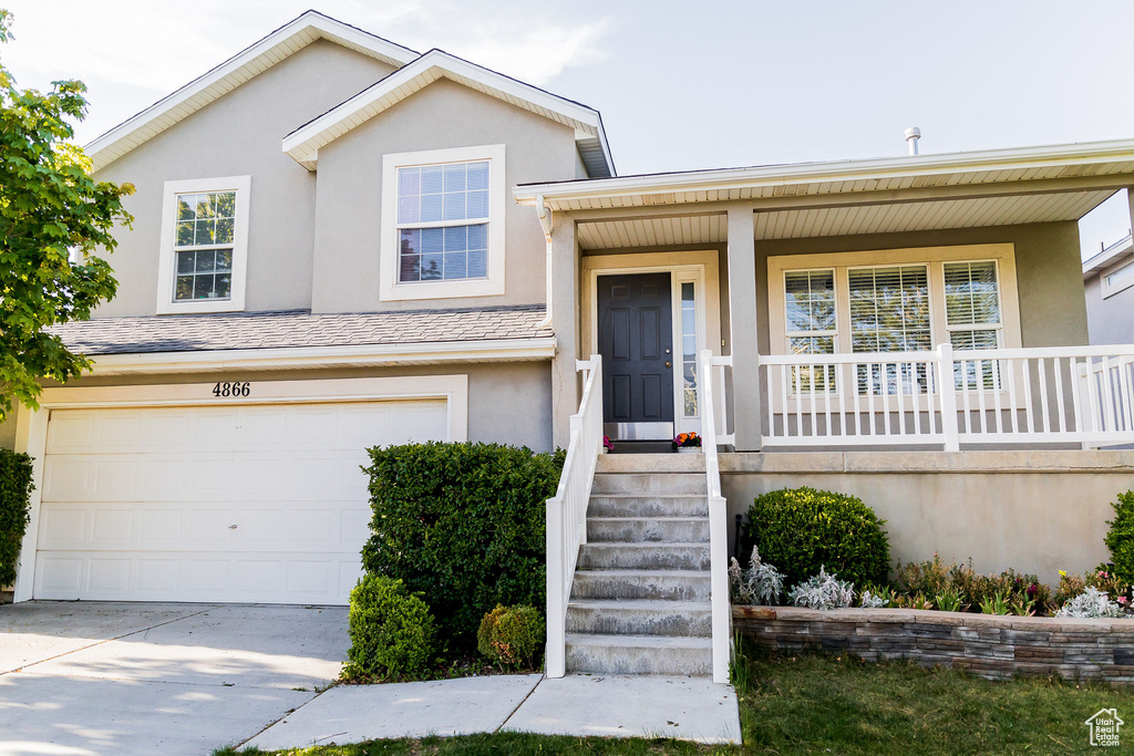 Tri-level home featuring covered porch, a garage, concrete driveway, and stucco siding