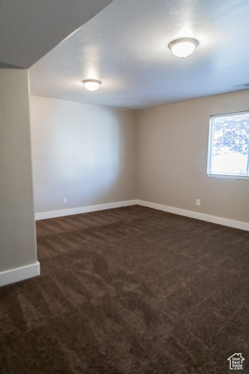 Empty room featuring baseboards, visible vents, and dark colored carpet