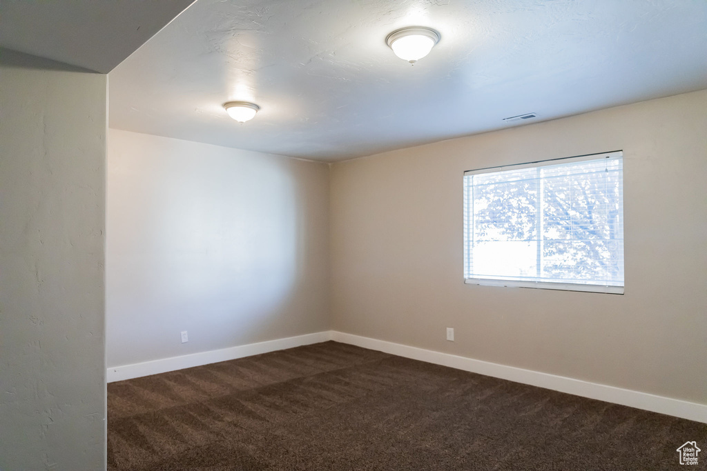 Spare room with baseboards, dark colored carpet, and visible vents