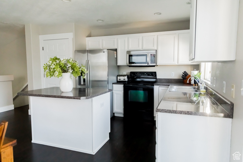 Kitchen featuring white cabinets, dark wood-style flooring, appliances with stainless steel finishes, a sink, and a center island