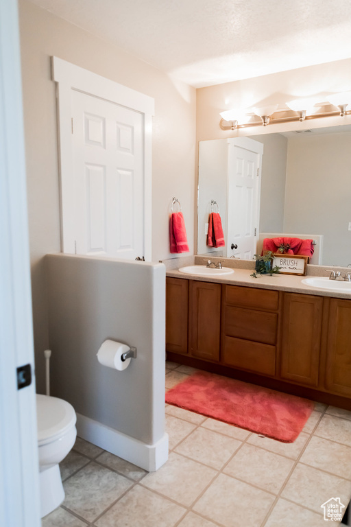 Bathroom with double vanity, toilet, a sink, and tile patterned flooring
