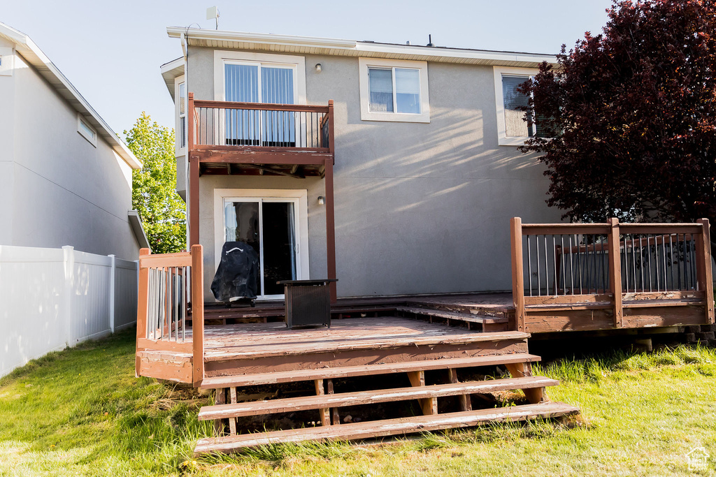 Back of property with a lawn, a deck, fence, a balcony, and stucco siding