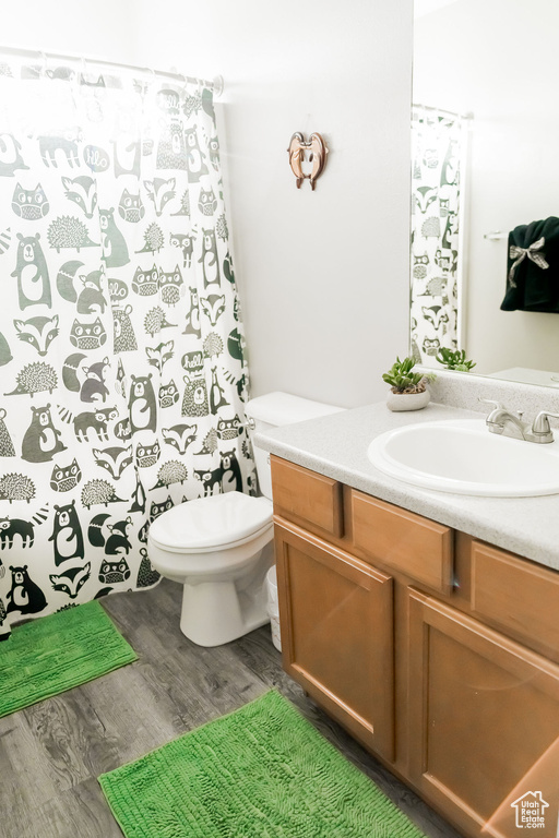 Bathroom with toilet, curtained shower, wood finished floors, and vanity