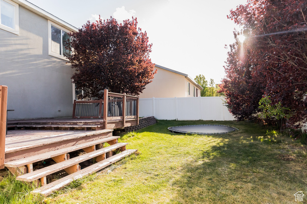 View of yard with a trampoline, a wooden deck, and fence