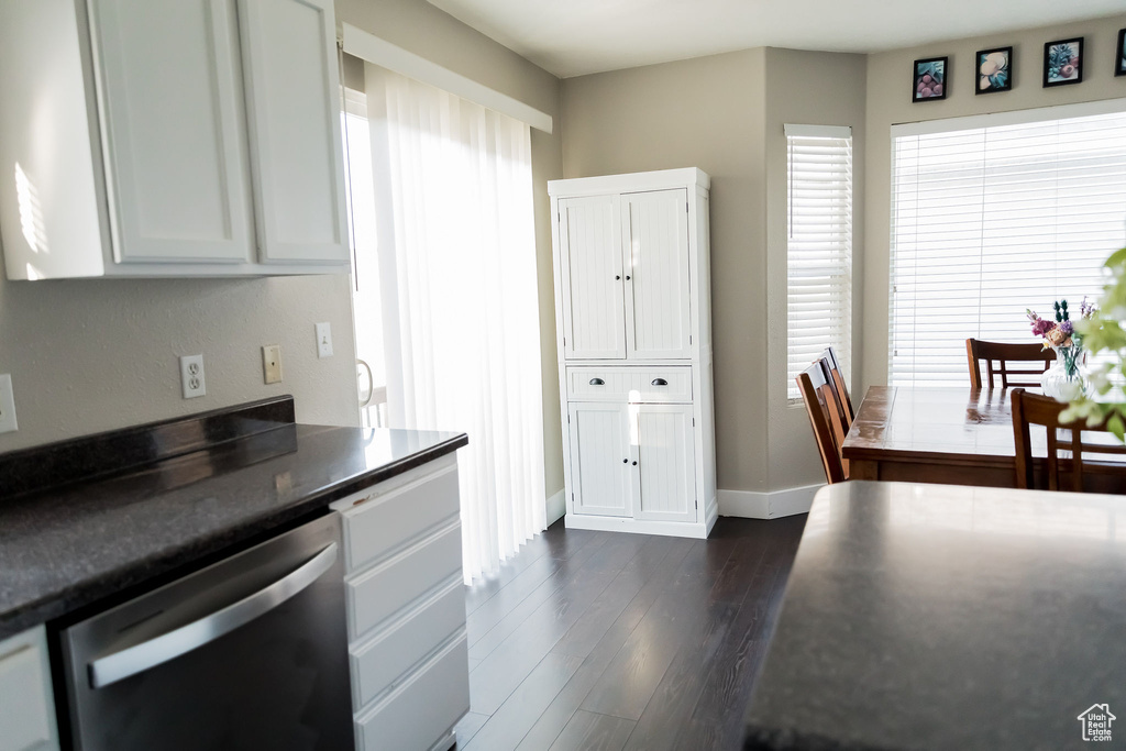 Kitchen featuring dark countertops, stainless steel dishwasher, baseboards, dark wood-style floors, and white cabinetry