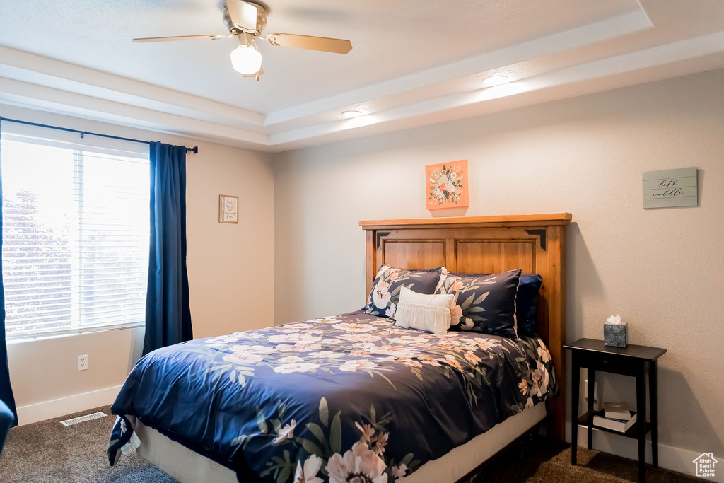 Bedroom with carpet flooring, ceiling fan, a raised ceiling, baseboards, and visible vents