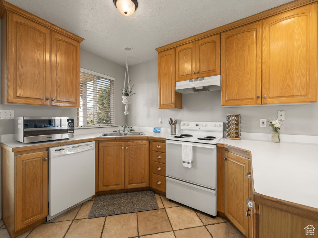 Kitchen featuring brown cabinets, a sink, light countertops, under cabinet range hood, and white appliances