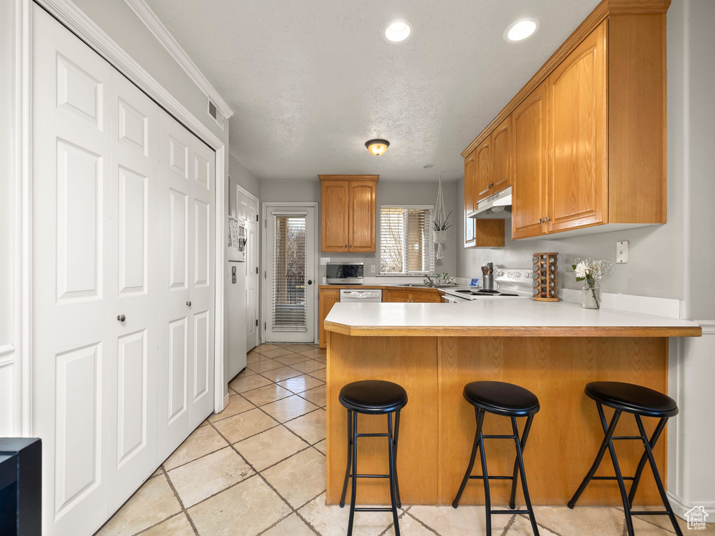 Kitchen with a peninsula, white appliances, a breakfast bar area, light countertops, and under cabinet range hood