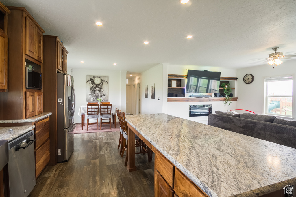 Kitchen featuring appliances with stainless steel finishes, dark wood finished floors, recessed lighting, brown cabinets, and light stone counters