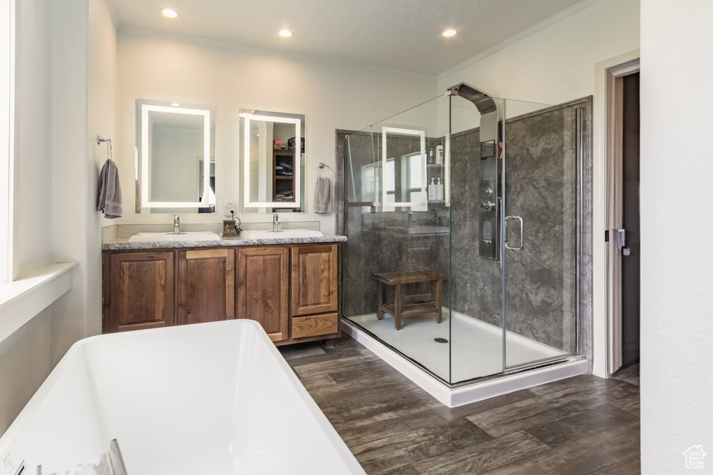Full bathroom featuring wood finished floors, a freestanding tub, double vanity, recessed lighting, and ornamental molding