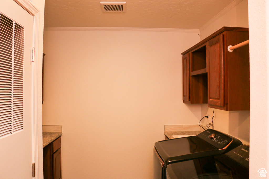 Clothes washing area featuring visible vents, a heating unit, crown molding, washer and dryer, and cabinet space