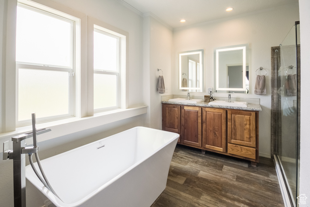Bathroom featuring a soaking tub, double vanity, wood finished floors, ornamental molding, and a stall shower
