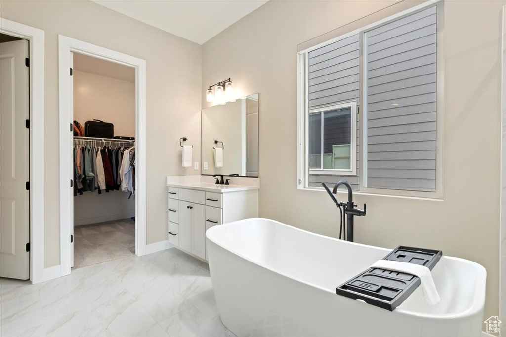 Full bath with marble finish flooring, vanity, a soaking tub, a walk in closet, and baseboards