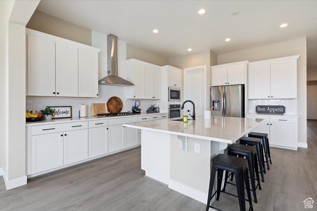 Kitchen featuring stainless steel appliances, wall chimney range hood, backsplash, white cabinets, and recessed lighting