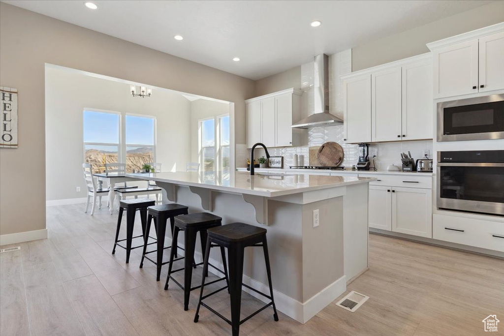 Kitchen with wall chimney range hood, a breakfast bar area, stainless steel appliances, tasteful backsplash, and a center island with sink