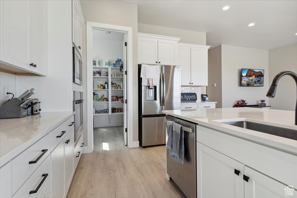 Kitchen featuring a sink, white cabinets, stainless steel appliances, recessed lighting, and light wood-style flooring