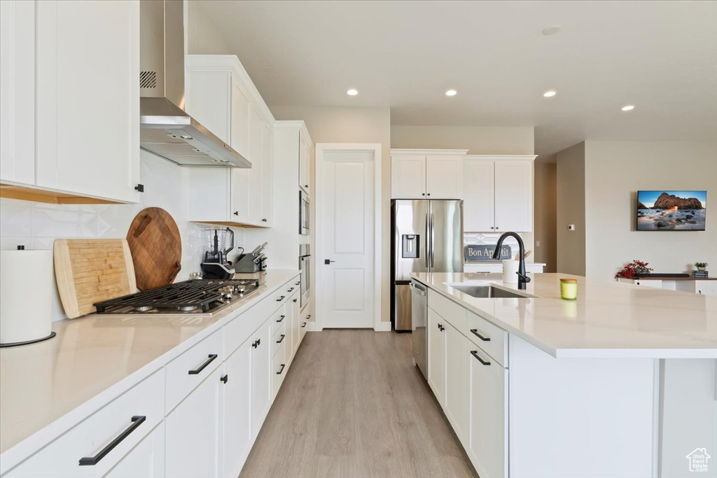 Kitchen with a sink, wall chimney exhaust hood, appliances with stainless steel finishes, light wood-style flooring, and decorative backsplash