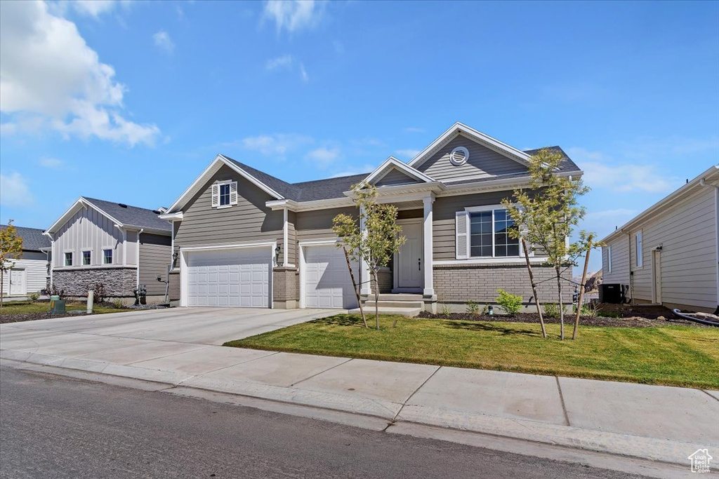 View of front of home featuring an attached garage, driveway, a front yard, and cooling unit