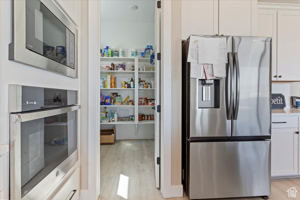 Kitchen with stainless steel appliances, light wood finished floors, and white cabinets