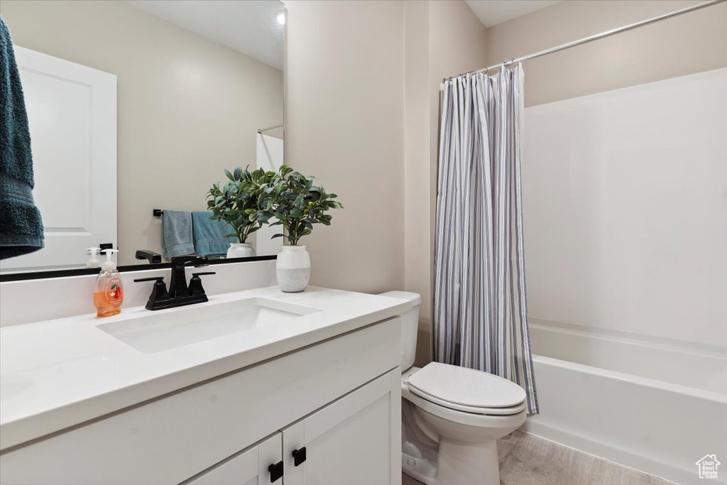 Bathroom with vanity, shower / bathtub combination with curtain, wood finished floors, and toilet
