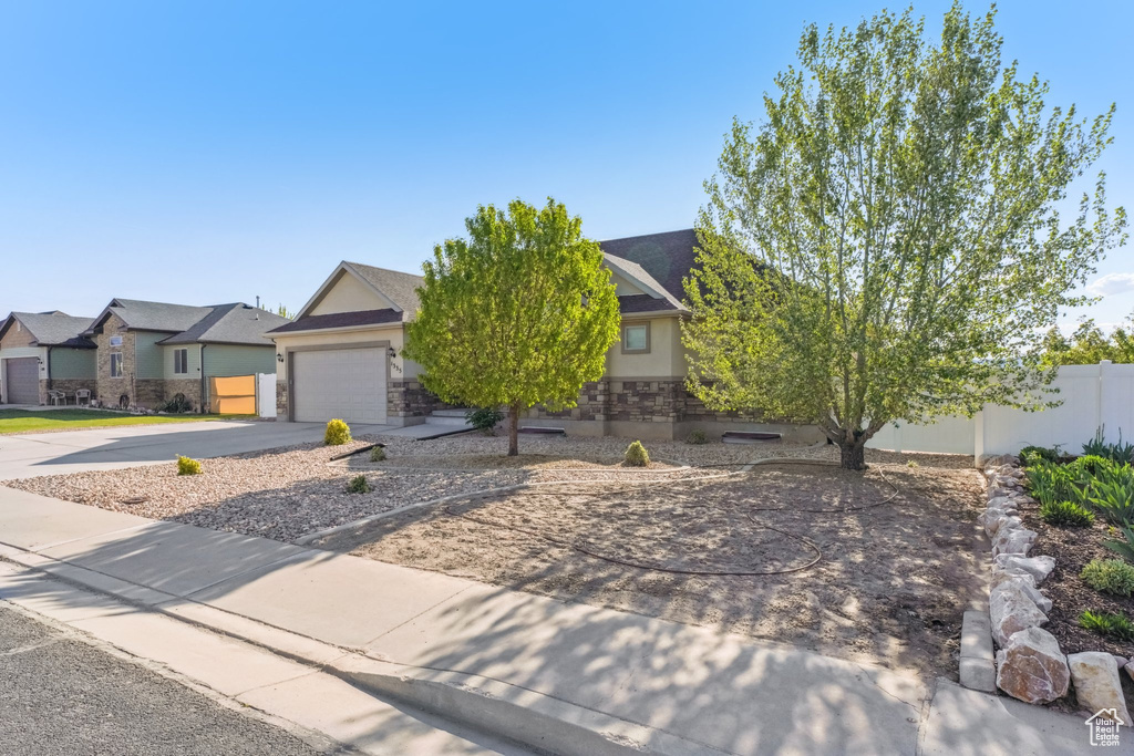 View of front of house with stucco siding, driveway, stone siding, and fence