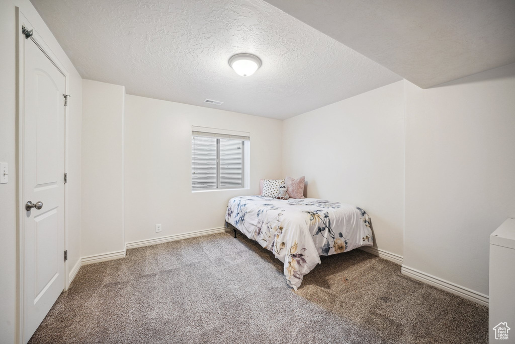 Carpeted bedroom featuring visible vents, a textured ceiling, and baseboards