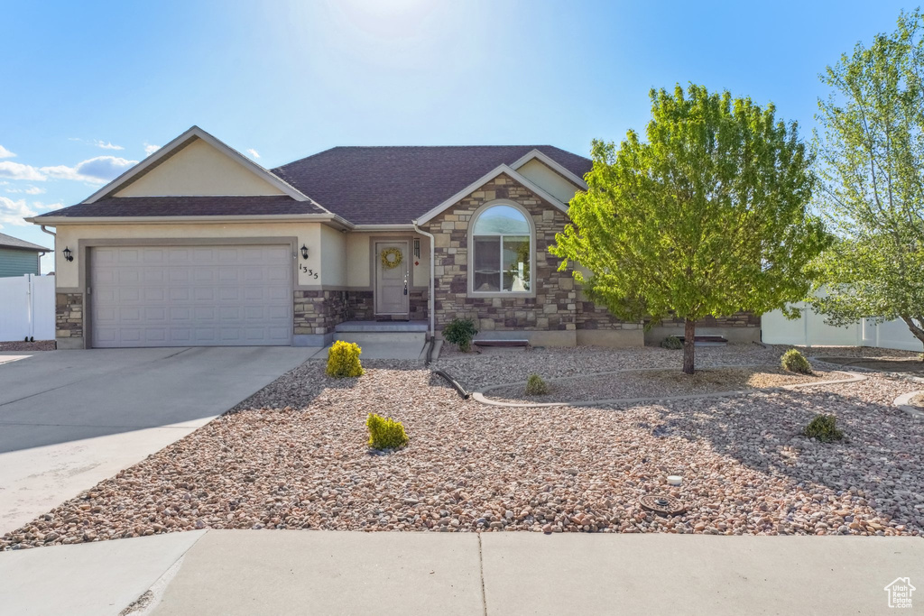 View of front of home with a garage, stone siding, stucco siding, a shingled roof, and concrete driveway