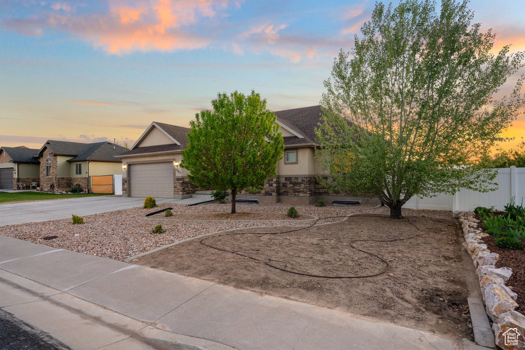 View of front facade featuring a garage, fence, stone siding, stucco siding, and concrete driveway