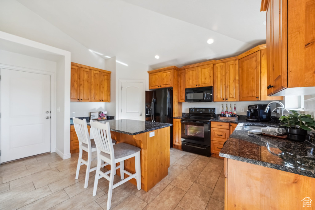 Kitchen featuring a breakfast bar, a sink, dark stone counters, vaulted ceiling, and black appliances
