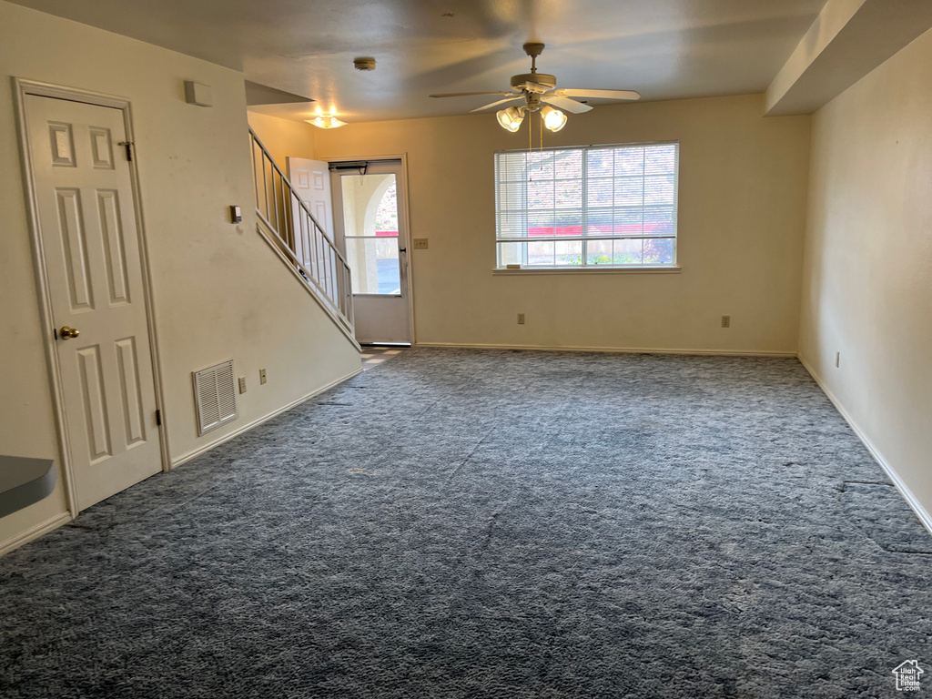 Unfurnished living room with carpet flooring, a ceiling fan, visible vents, and stairs