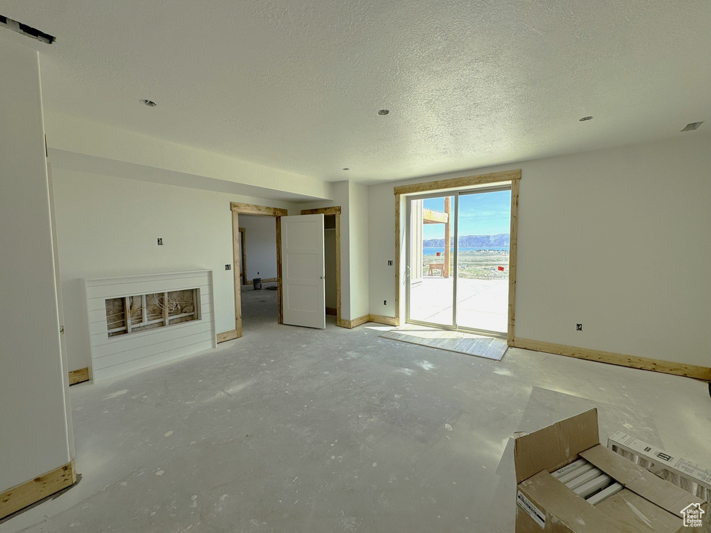 Unfurnished living room with unfinished concrete floors, a fireplace, and a textured ceiling