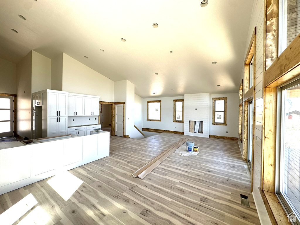Unfurnished living room featuring baseboards, high vaulted ceiling, a healthy amount of sunlight, and light wood-style floors