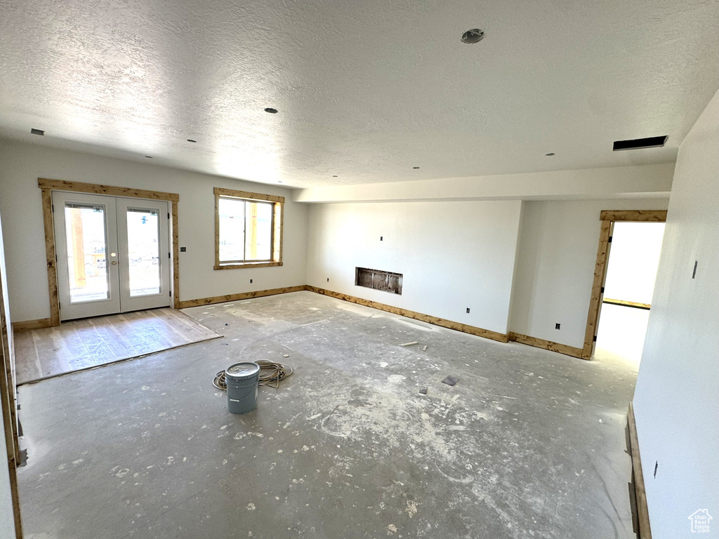 Unfurnished living room with baseboards, a textured ceiling, a fireplace, and french doors