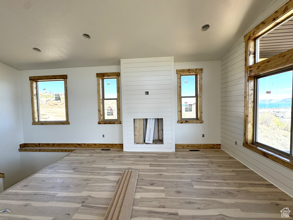 Unfurnished living room with a healthy amount of sunlight, light wood-style floors, and wooden walls