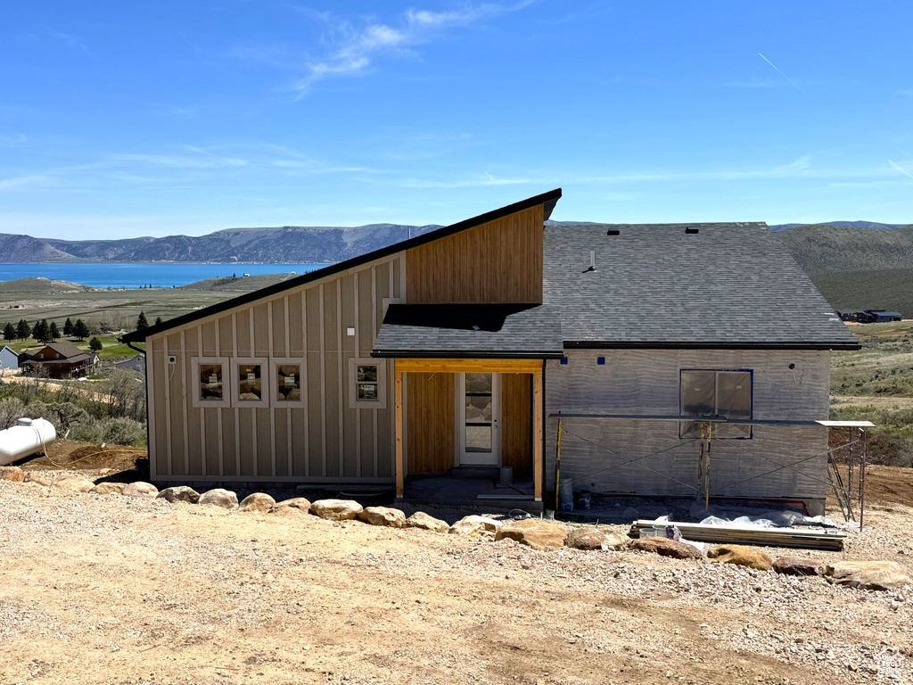 View of front facade featuring board and batten siding, roof with shingles, and a water and mountain view