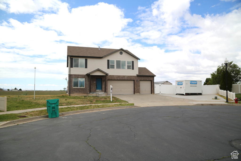 View of front of property featuring driveway, fence, brick siding, and an attached garage