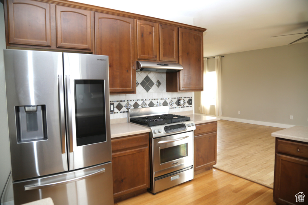 Kitchen with appliances with stainless steel finishes, under cabinet range hood, light wood-style floors, backsplash, and light countertops