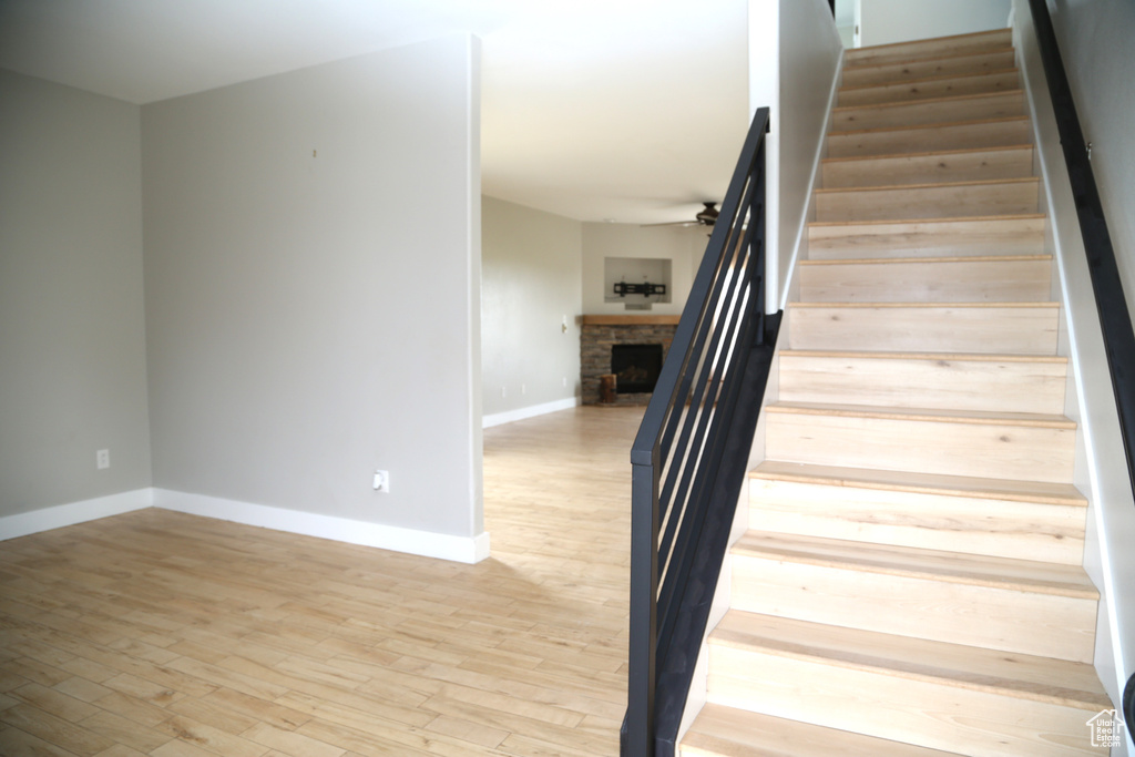 Staircase with wood finished floors, a stone fireplace, baseboards, and a ceiling fan