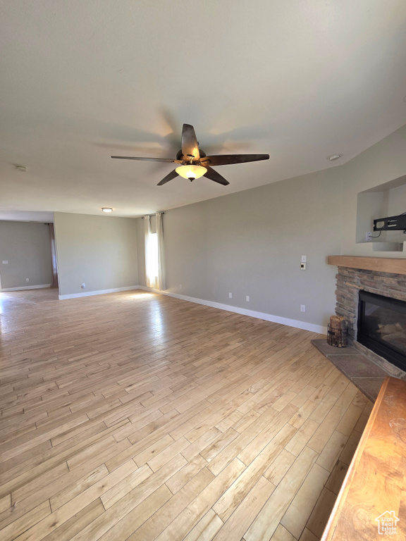 Unfurnished living room featuring ceiling fan, light wood-type flooring, a stone fireplace, and baseboards