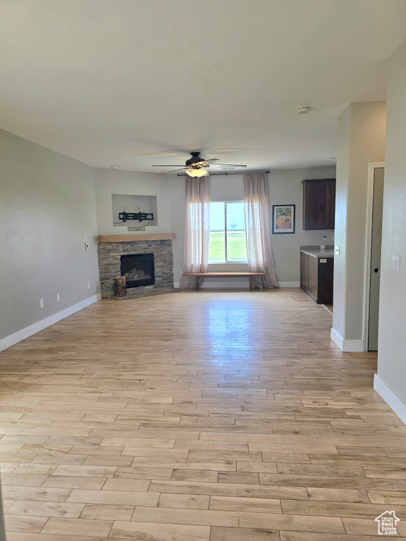 Unfurnished living room featuring light wood-style floors, a ceiling fan, baseboards, and a stone fireplace